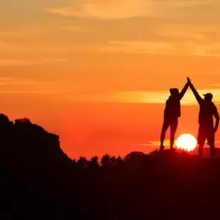 Silhouette of couple doing high 5s against a sunset backdrop