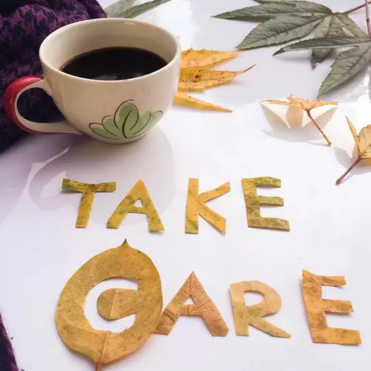 Cup of tea on table with take care written in cut out letters on top of table