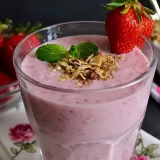 a fresh fruit smoothie topped with granola, mint, and strawberries 