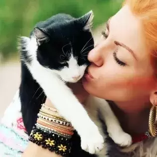 A woman kissing her black & white cat.