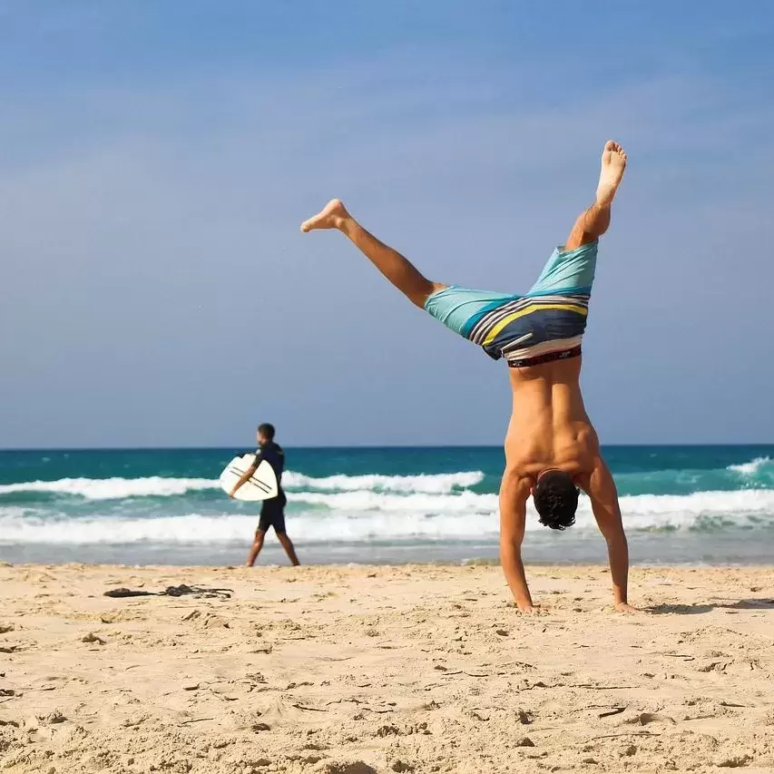 Man doing a cartwheel in the sand at a beach.